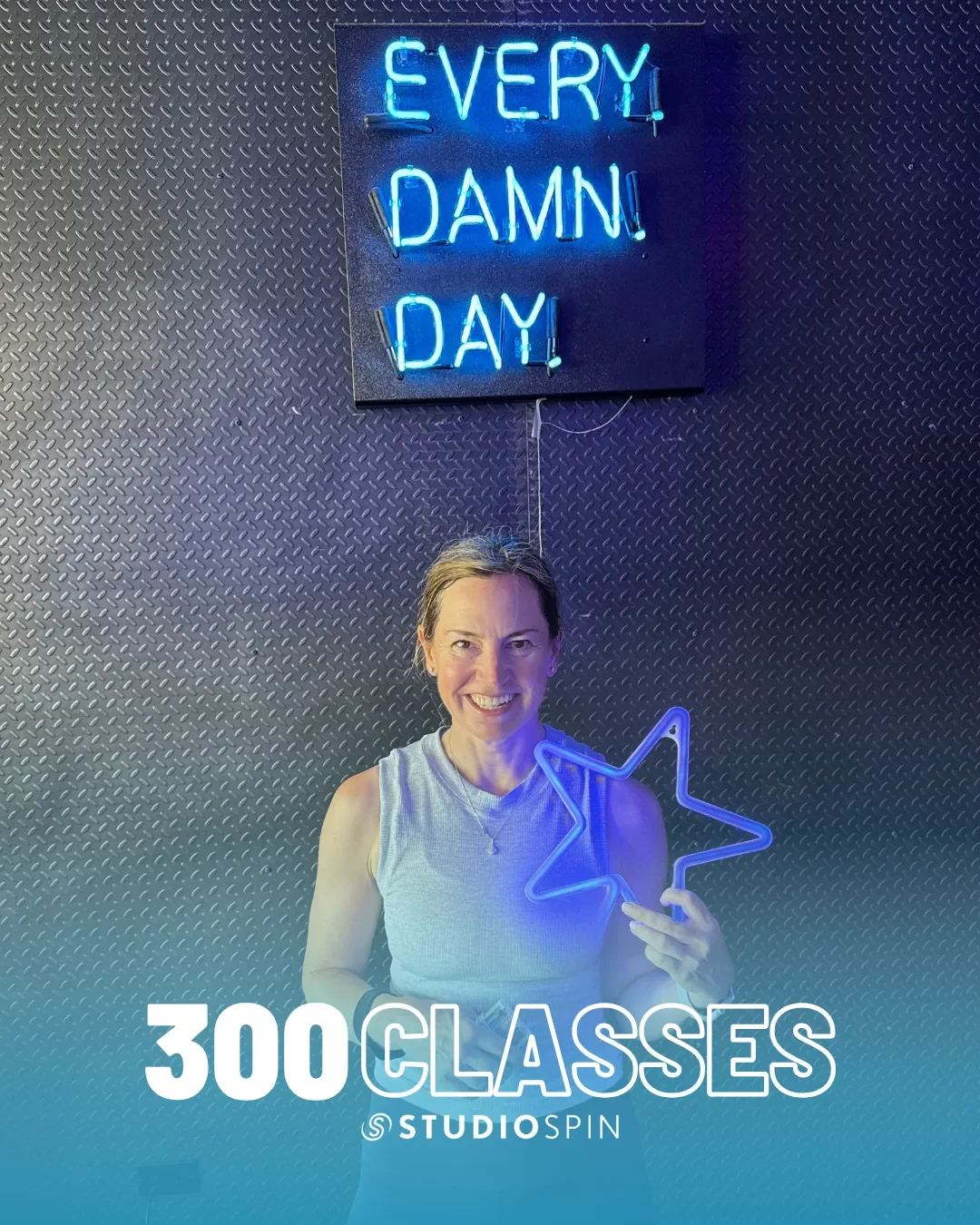 A Studio Spin member celebrating 300 classes under the Every Damn Day neon sign.
