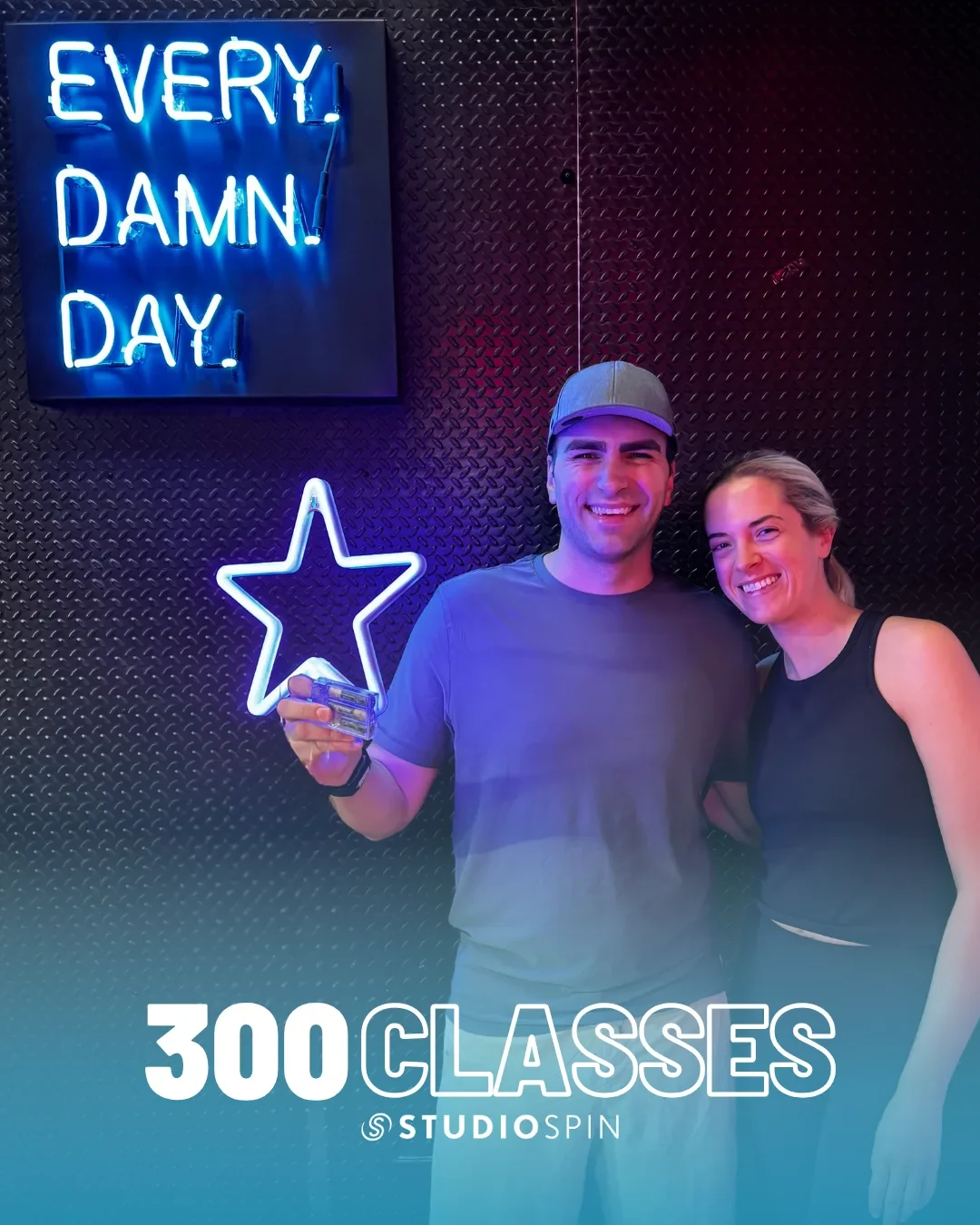 A Studio Spin member celebrating 300 classes under the Every Damn Day neon sign.