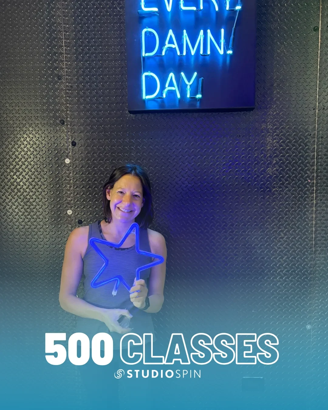 A Studio Spin member celebrating 500 classes under the Every Damn Day neon sign.