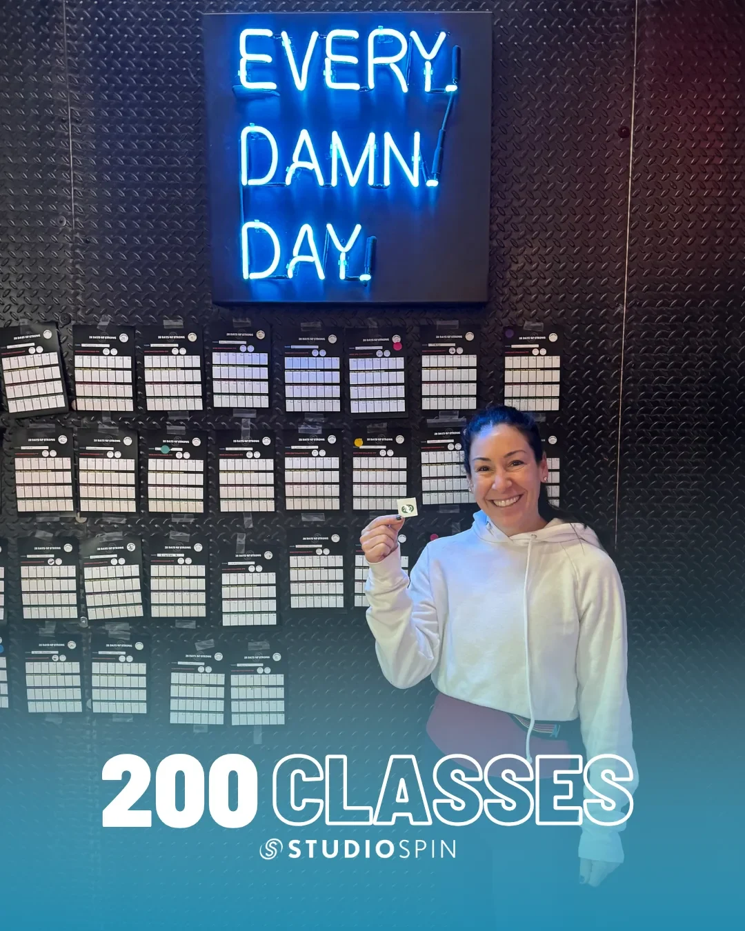A Studio Spin member celebrating 200 classes under the Every Damn Day neon sign.