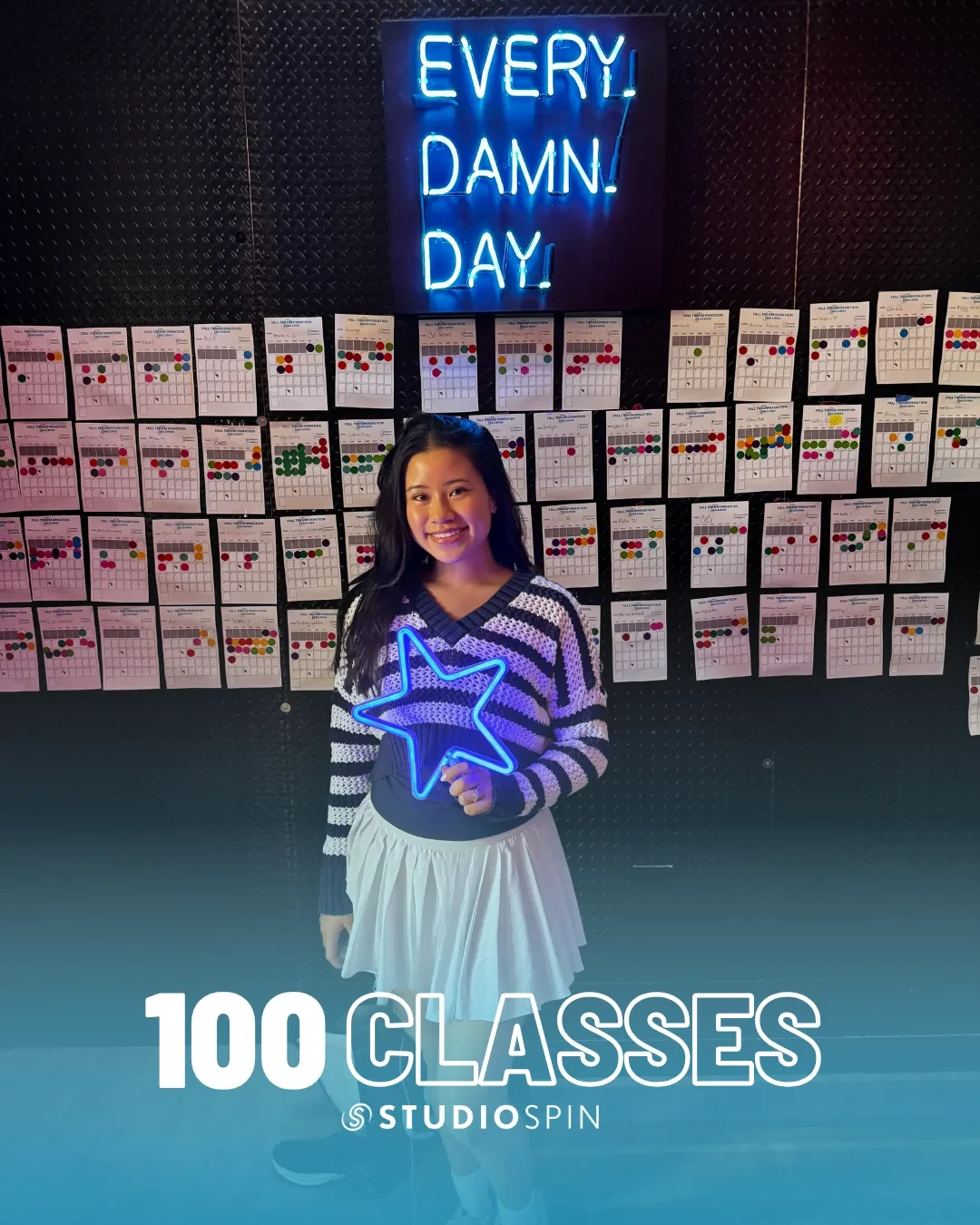 A Studio Spin member celebrating 100 classes under the Every Damn Day neon sign.