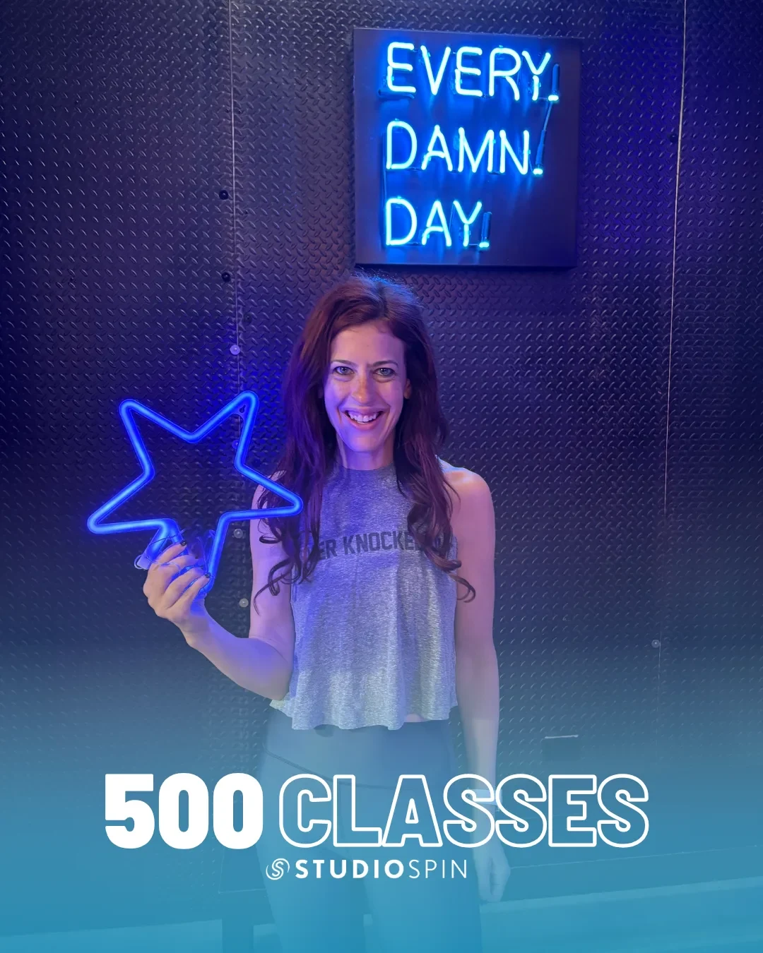 A Studio Spin member celebrating 500 classes under the Every Damn Day neon sign.