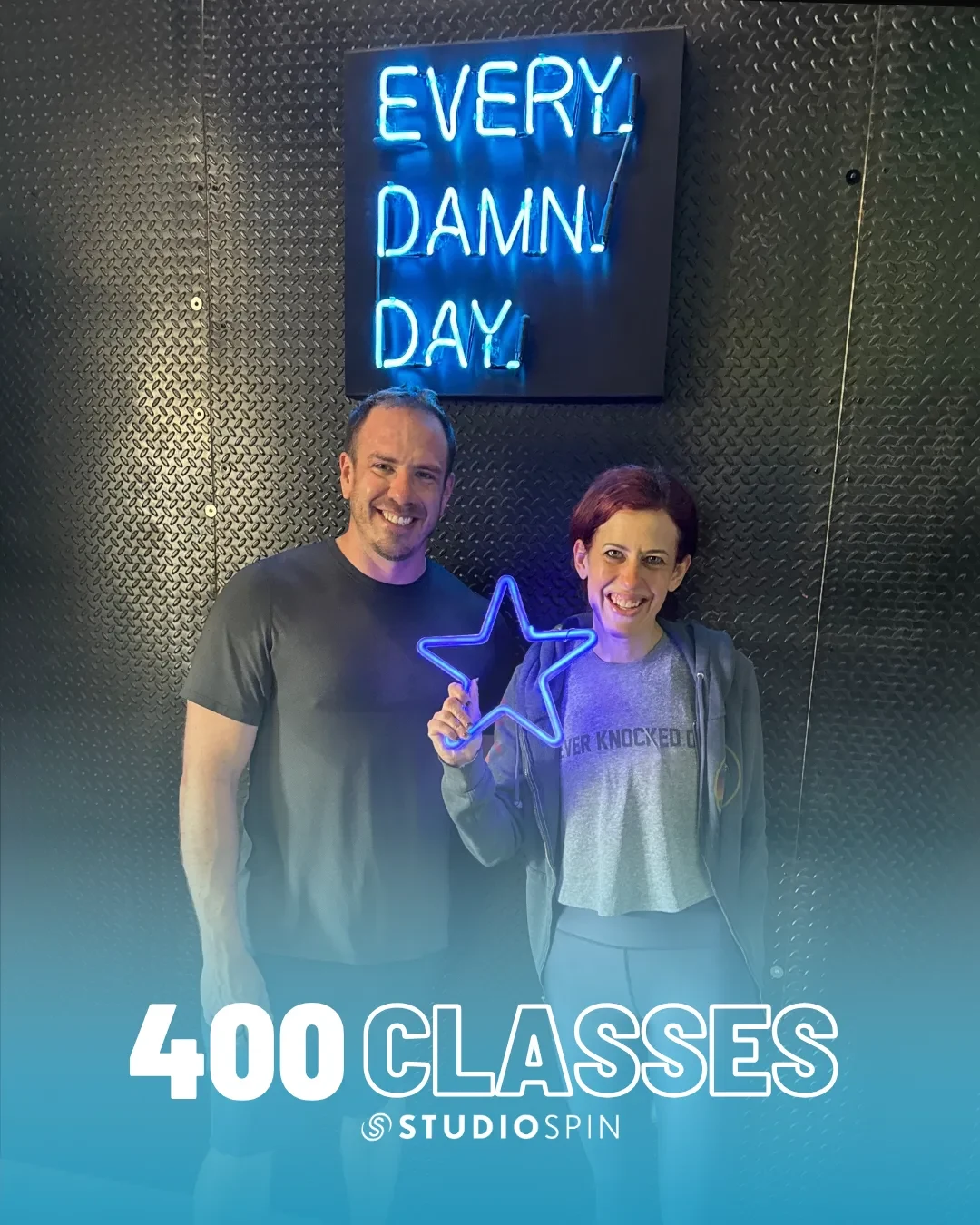 A Studio Spin member celebrating 400 classes under the Every Damn Day neon sign.