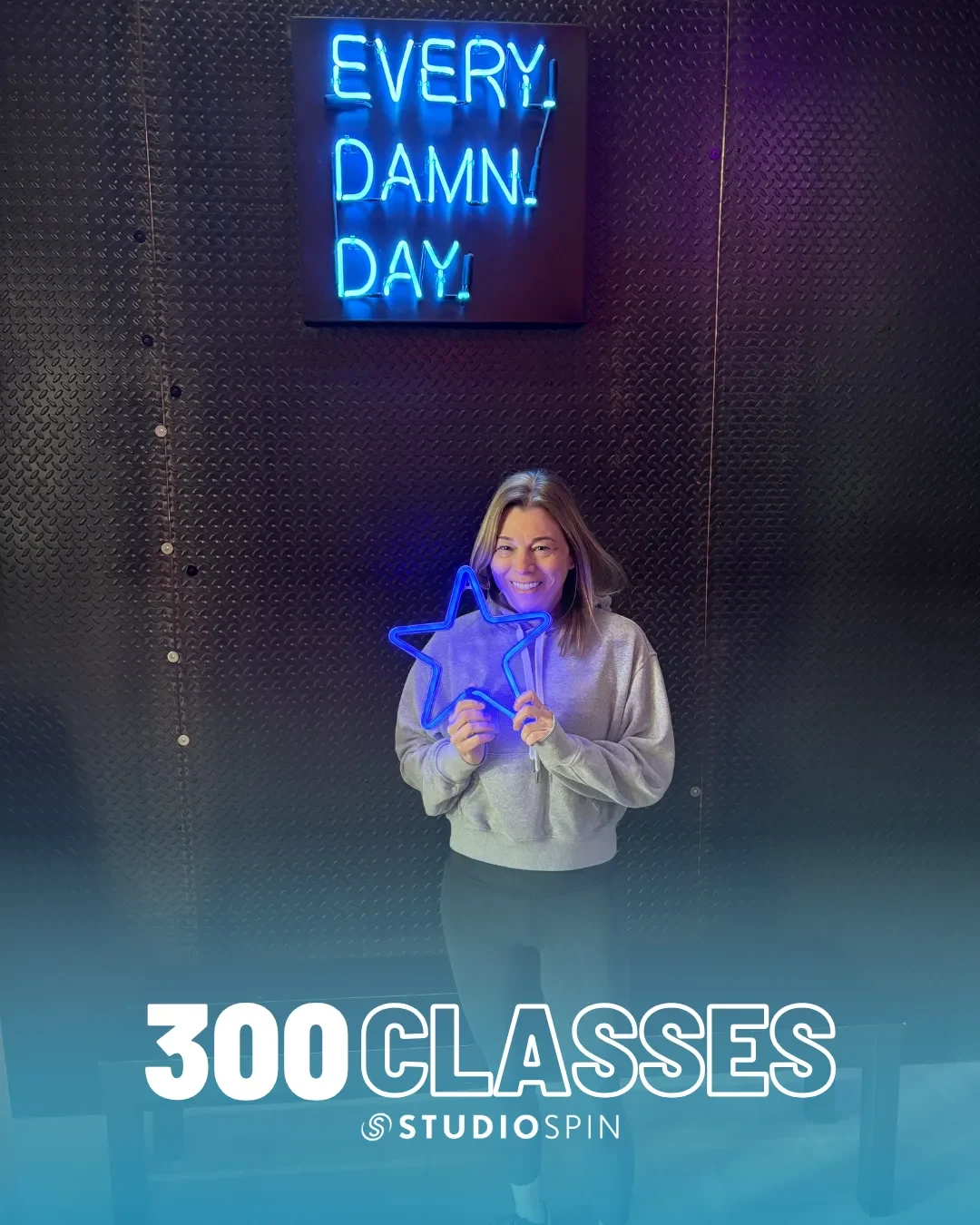 A Studio Spin member celebrating 300 classes under the Every Damn Day neon sign.