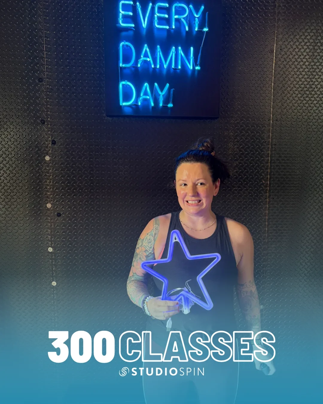 A Studio Spin member celebrating 300 classes under the Every Damn Day neon sign.