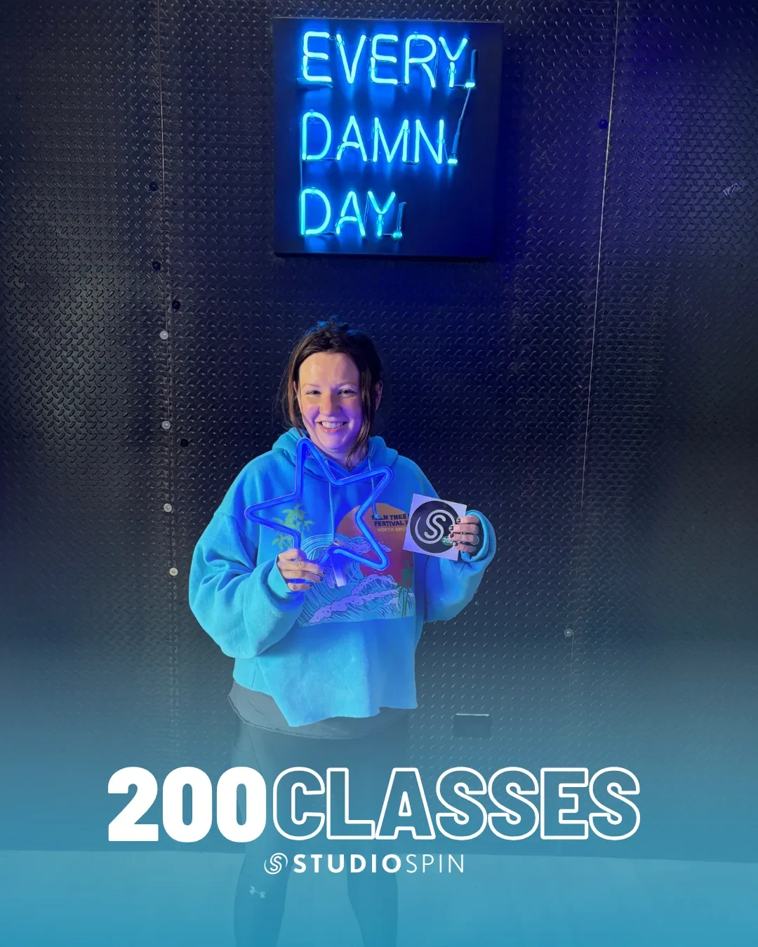 A Studio Spin member celebrating 200 classes under the Every Damn Day neon sign.
