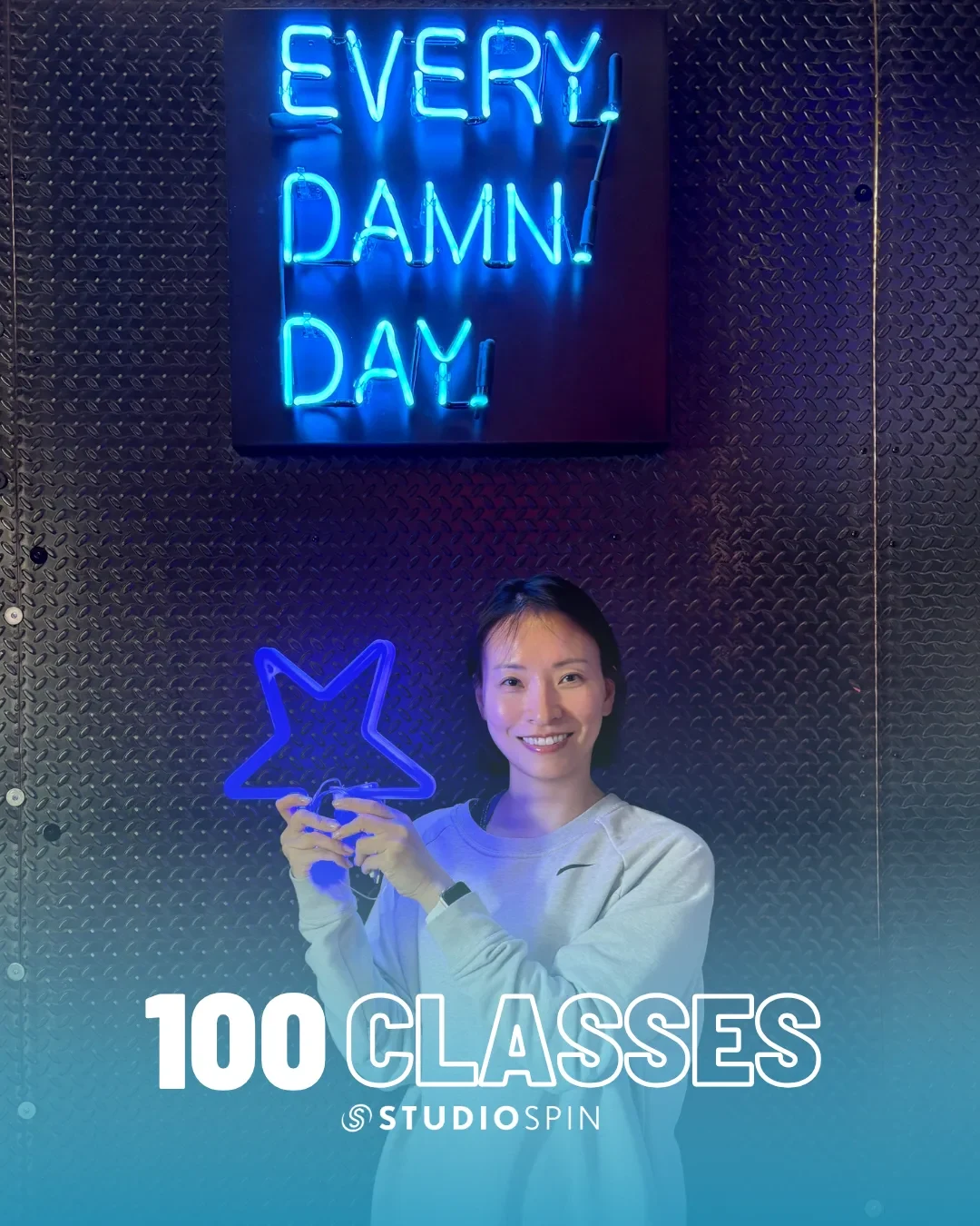 A Studio Spin member celebrating 100 classes under the Every Damn Day neon sign.