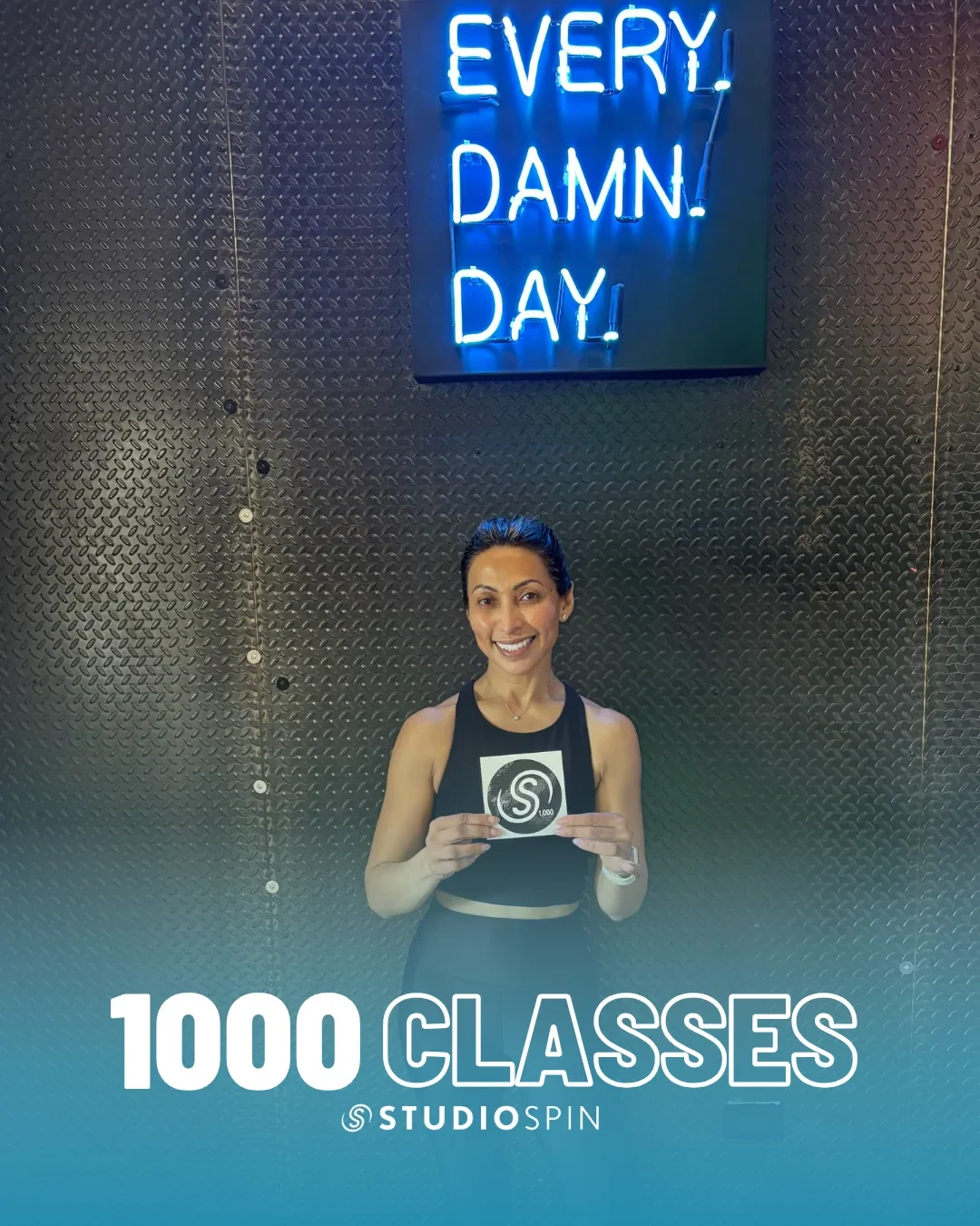 A Studio Spin member celebrating 1,000 classes under the Every Damn Day neon sign.