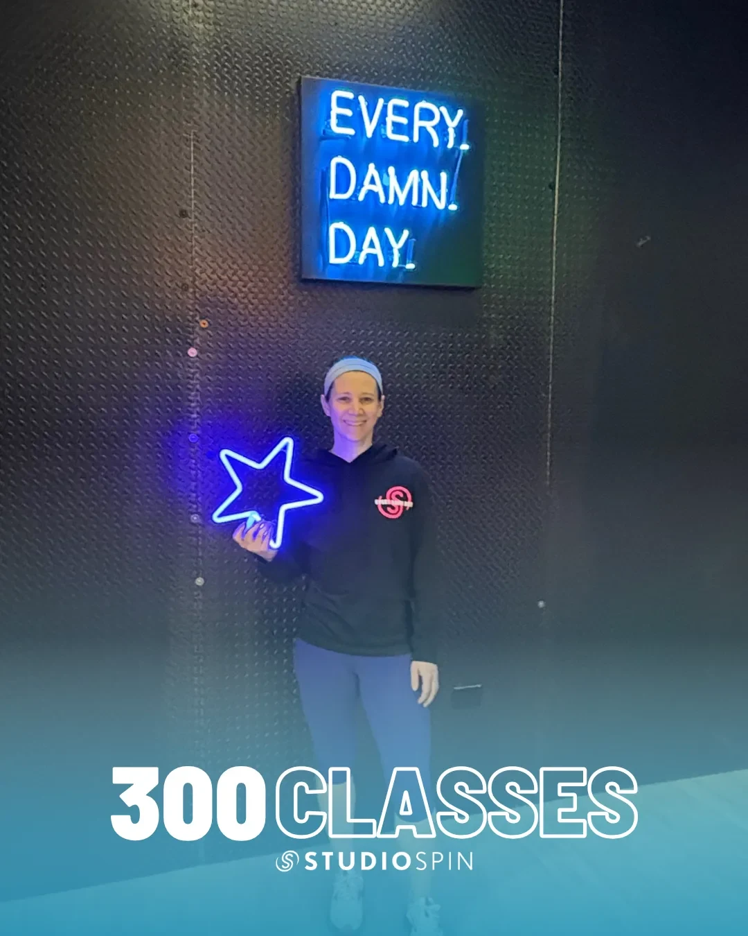 A Studio Spin member celebrating 300 classes under the Every Damn Day neon sign.