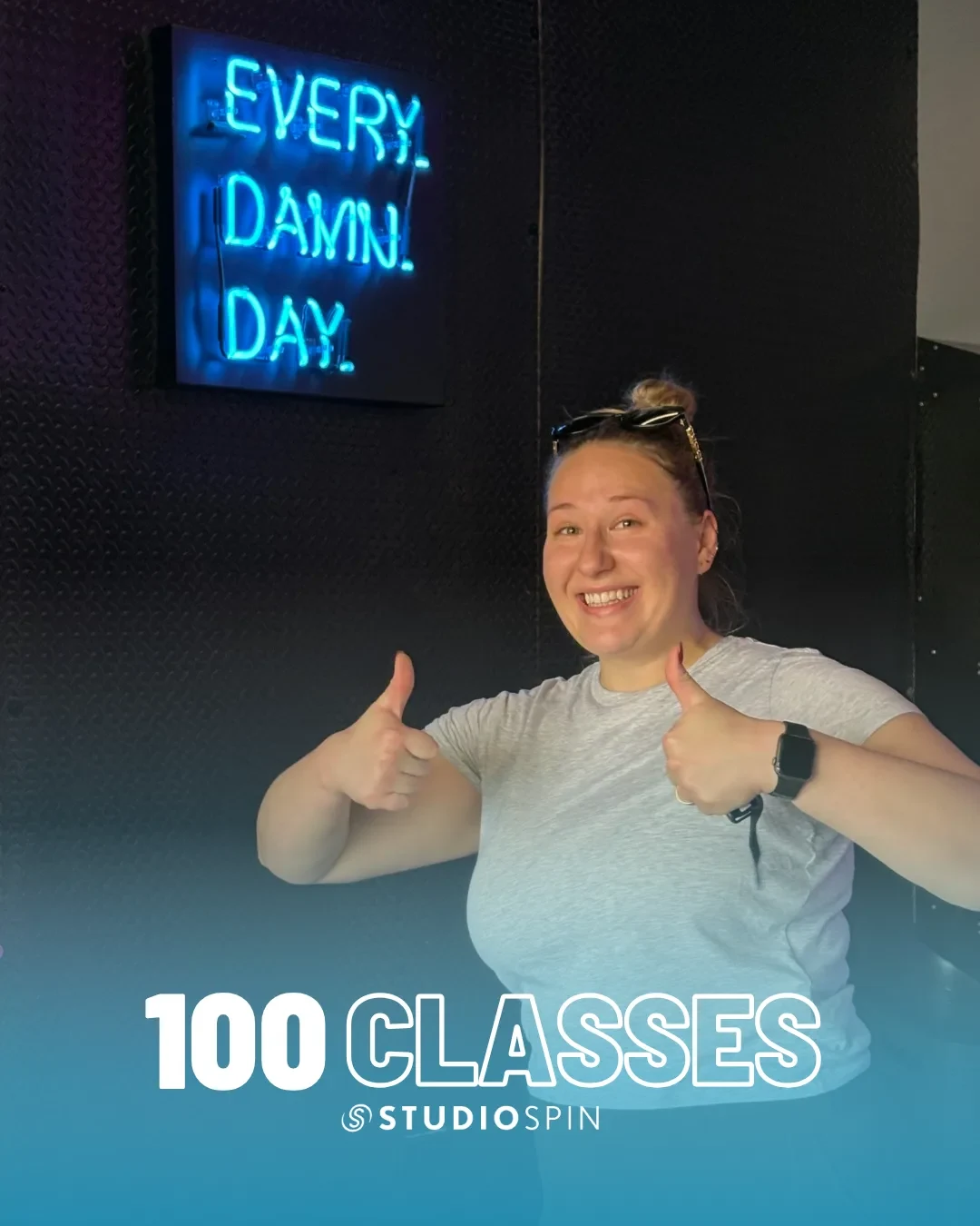 A Studio Spin member celebrating 100 classes under the Every Damn Day neon sign.