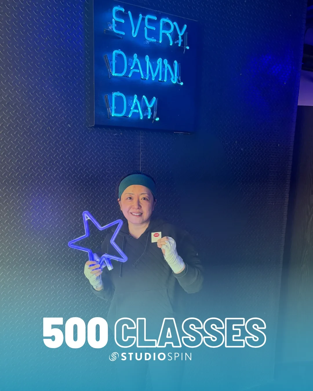 A Studio Spin member celebrating 500 classes under the Every Damn Day neon sign.