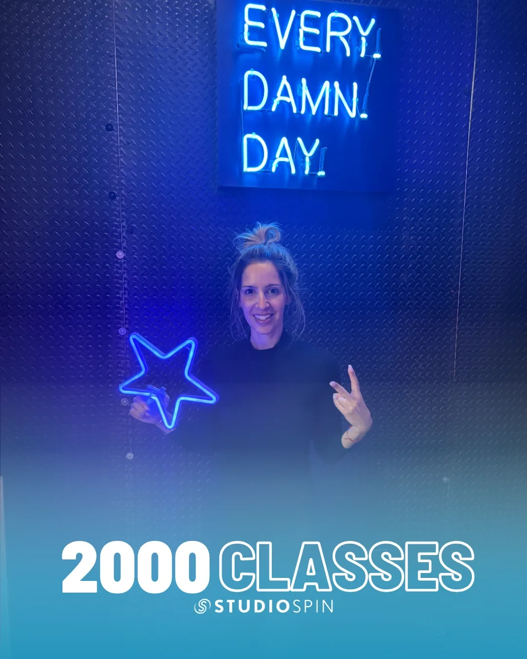 A Studio Spin member celebrating 2,000 classes under the Every Damn Day neon sign.