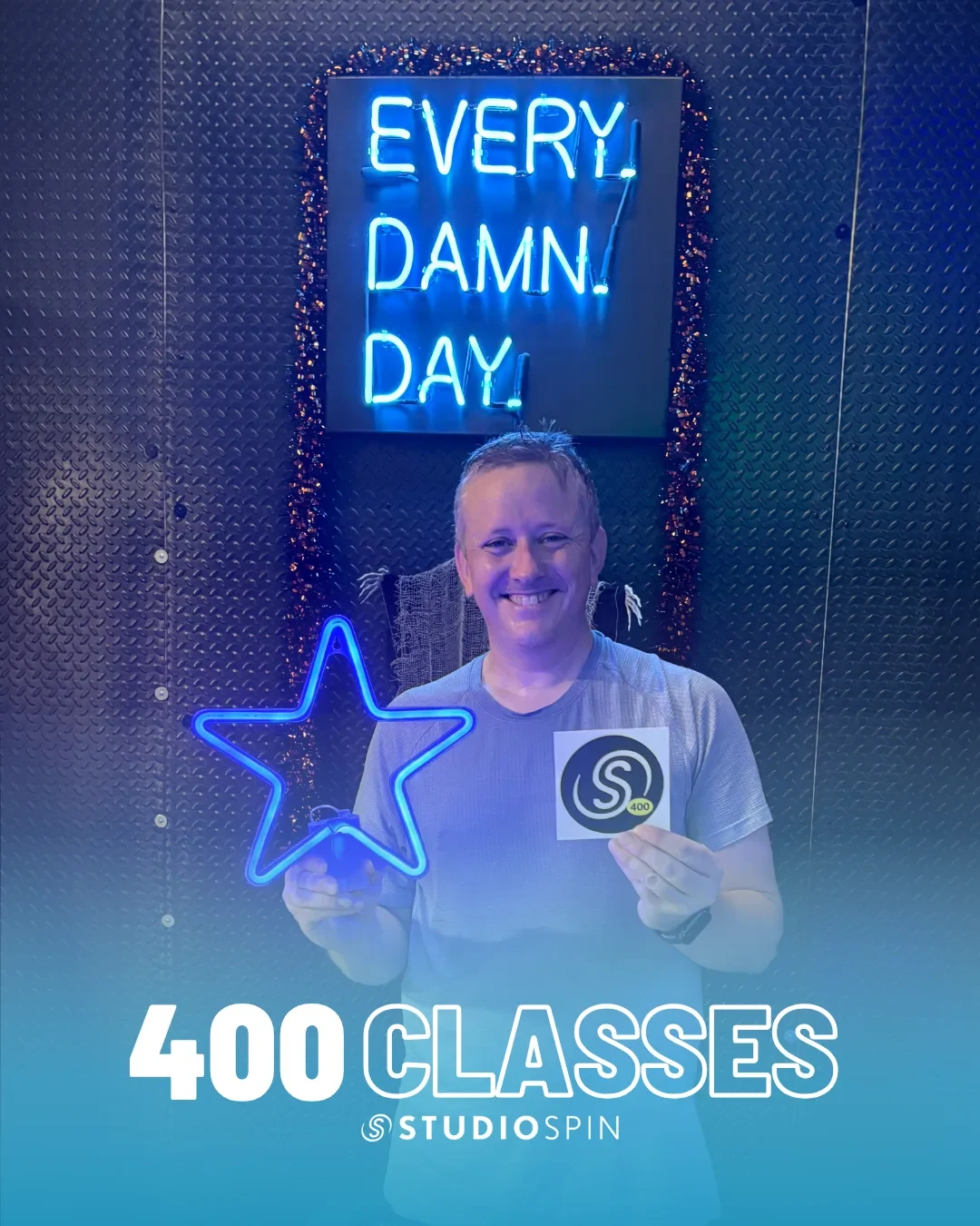 A Studio Spin member celebrating 400 classes under the Every Damn Day neon sign.