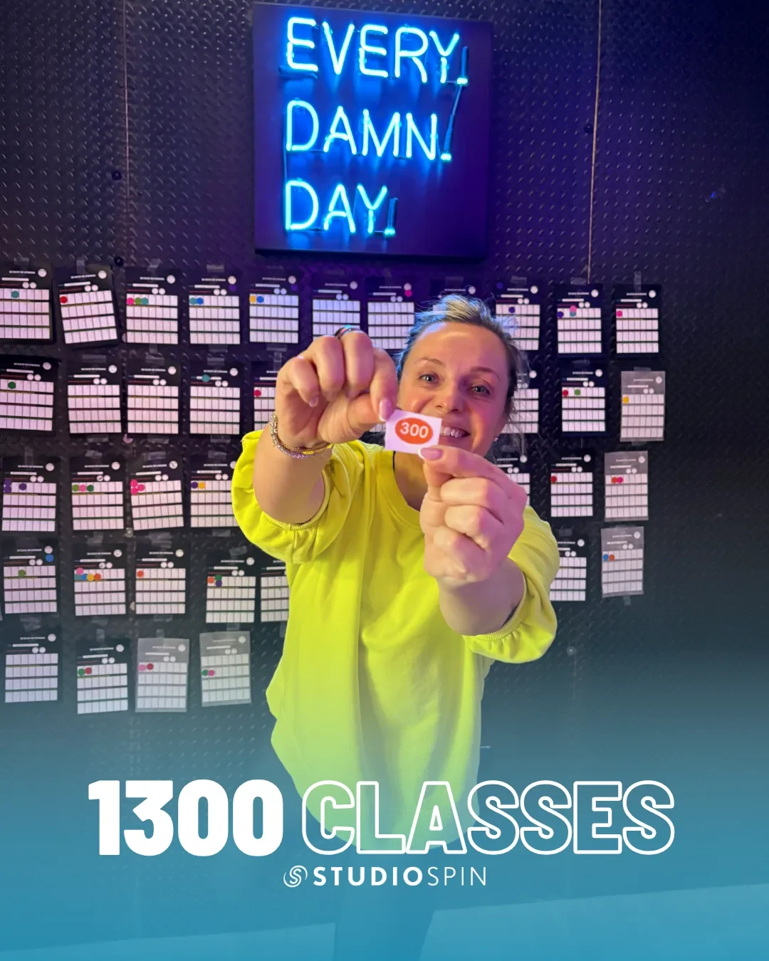 A Studio Spin member celebrating 1,300 classes under the Every Damn Day neon sign.