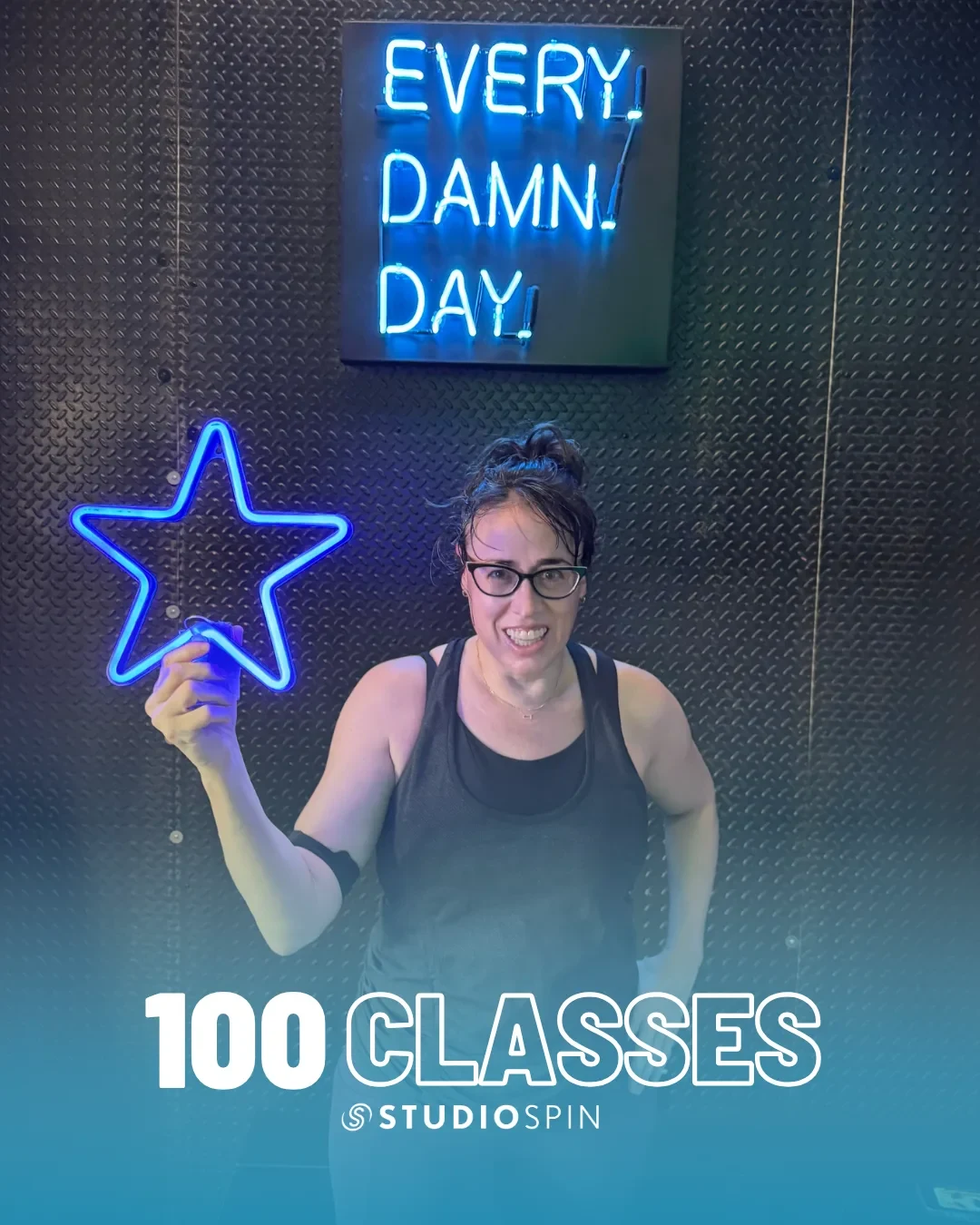 A Studio Spin member celebrating 100 classes under the Every Damn Day neon sign.