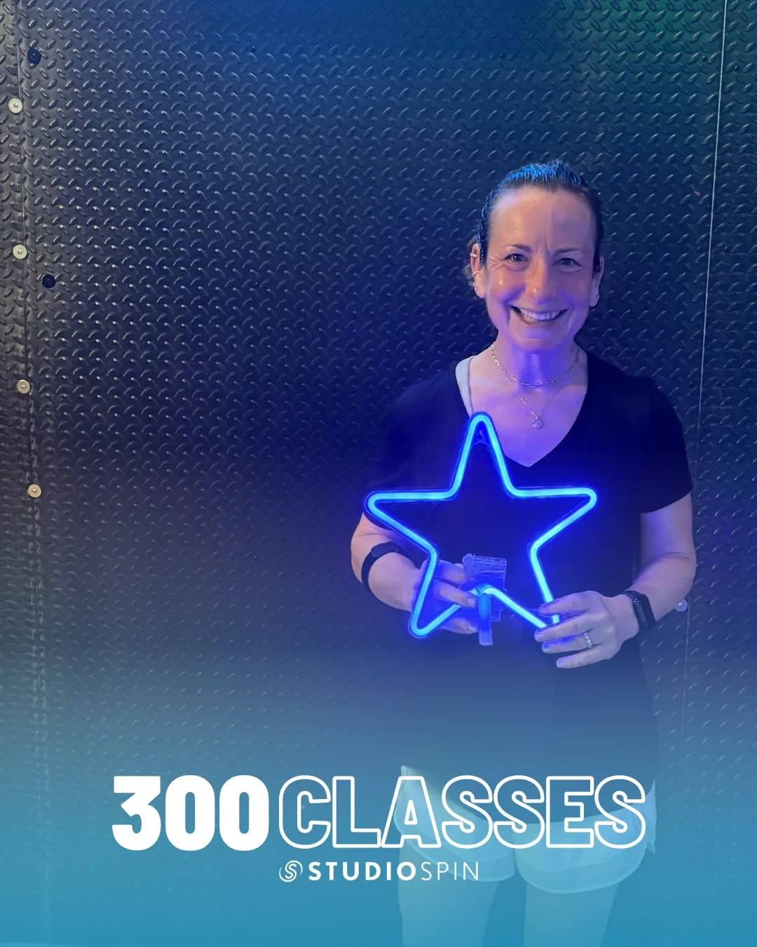A Studio Spin member celebrating 300 classes under the Every Damn Day neon sign.