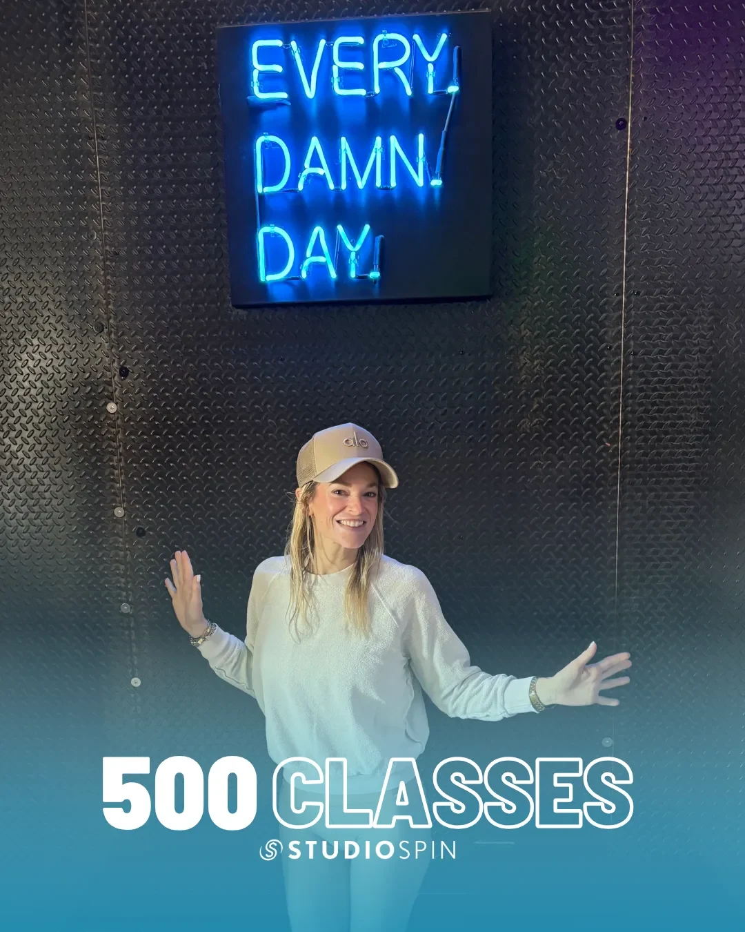 A Studio Spin member celebrating 500 classes under the Every Damn Day neon sign.
