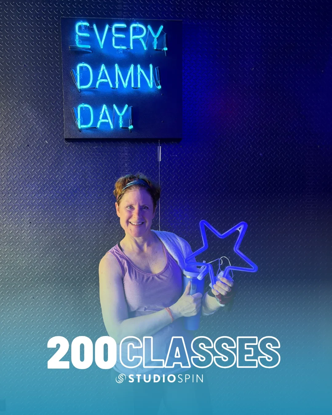 A Studio Spin member celebrating 200 classes under the Every Damn Day neon sign.