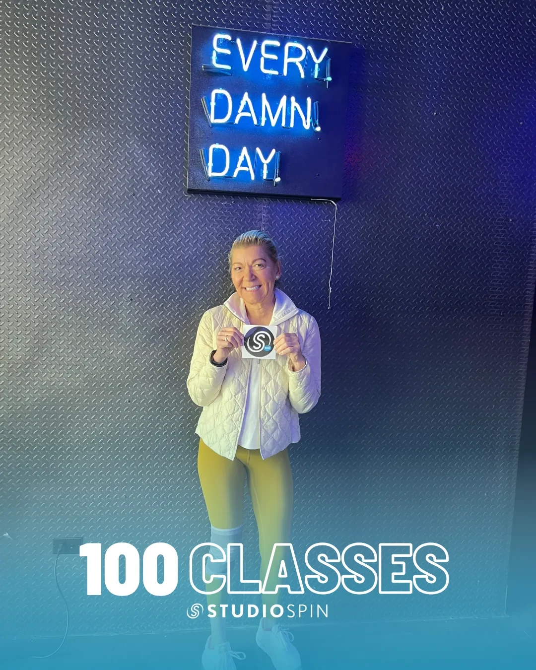 A Studio Spin member celebrating 100 classes under the Every Damn Day neon sign.