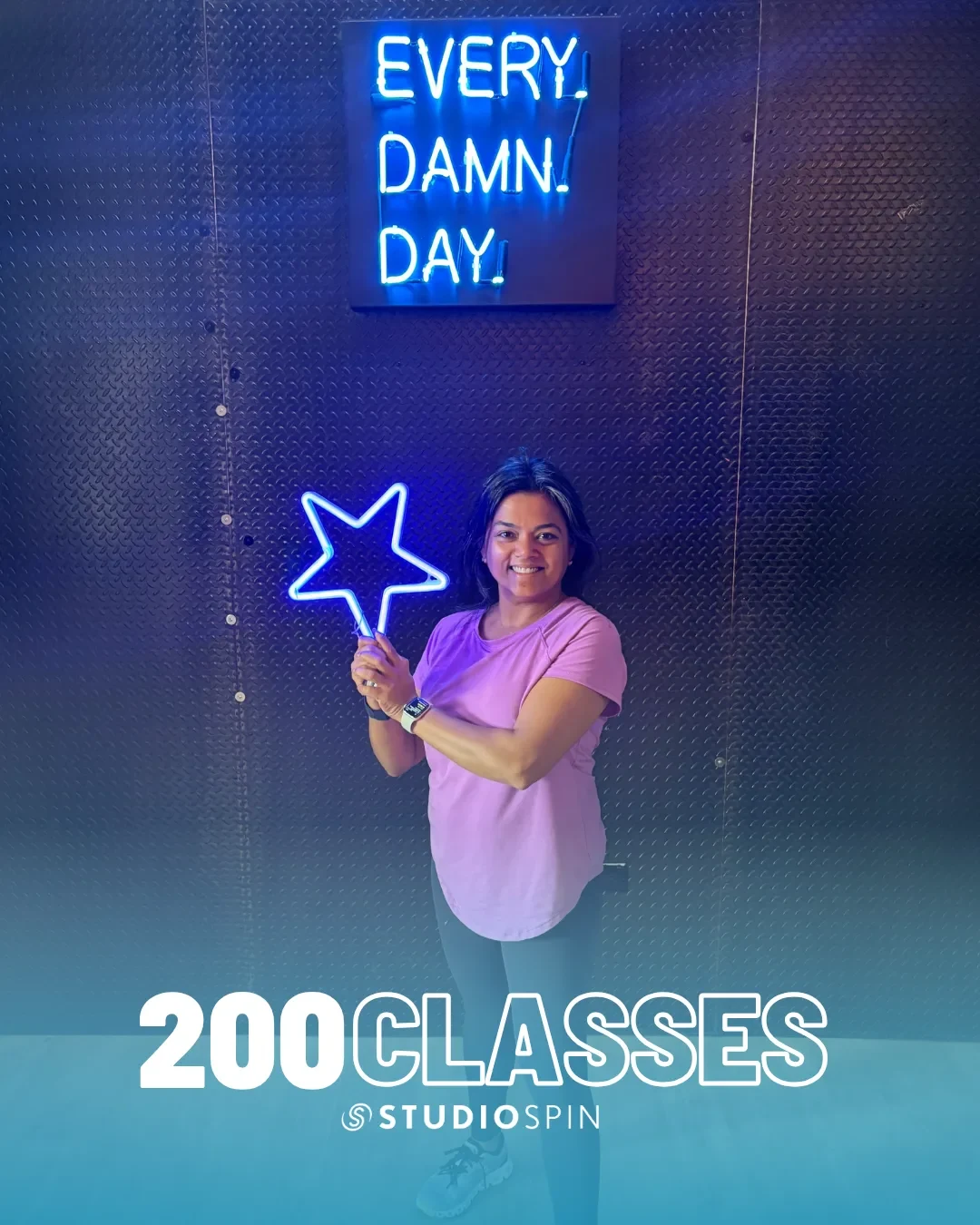 A Studio Spin member celebrating 200 classes under the Every Damn Day neon sign.