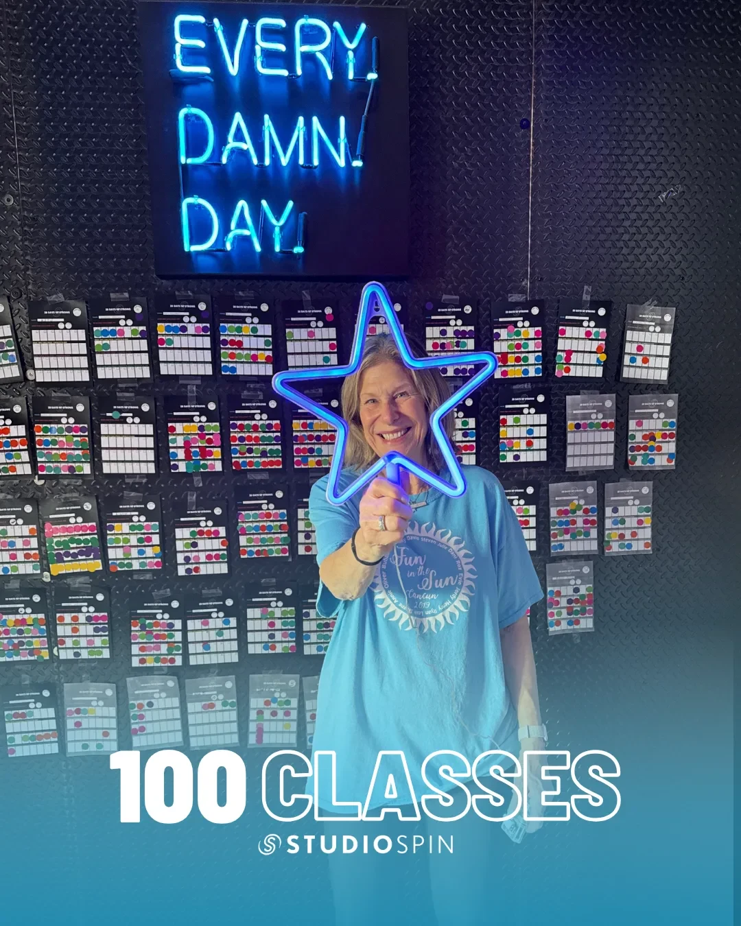 A Studio Spin member celebrating 100 classes under the Every Damn Day neon sign.