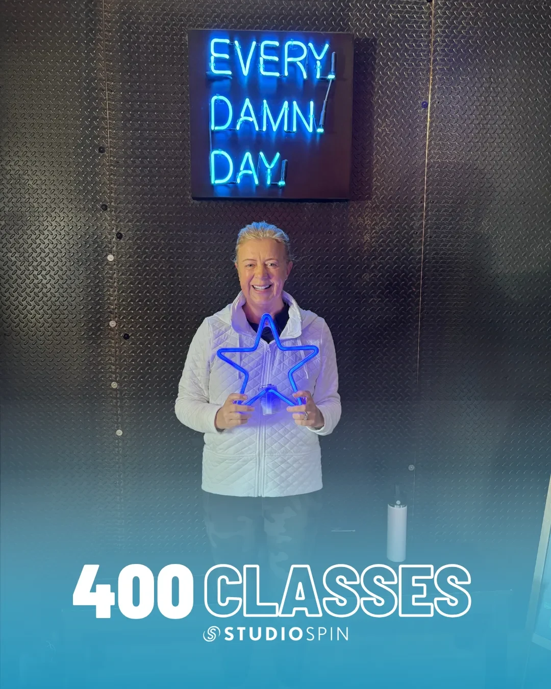 A Studio Spin member celebrating 400 classes under the Every Damn Day neon sign.