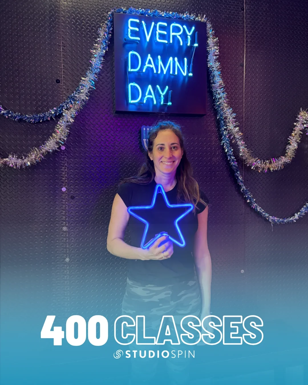 A Studio Spin member celebrating 400 classes under the Every Damn Day neon sign.