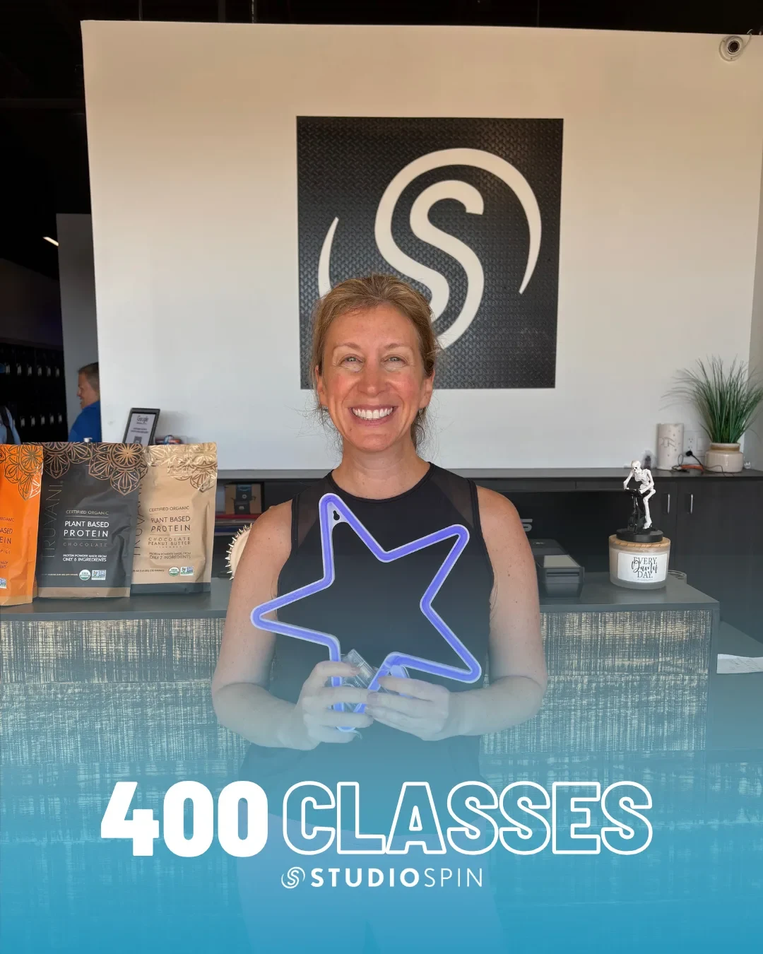 A Studio Spin member celebrating 400 classes under the Every Damn Day neon sign.
