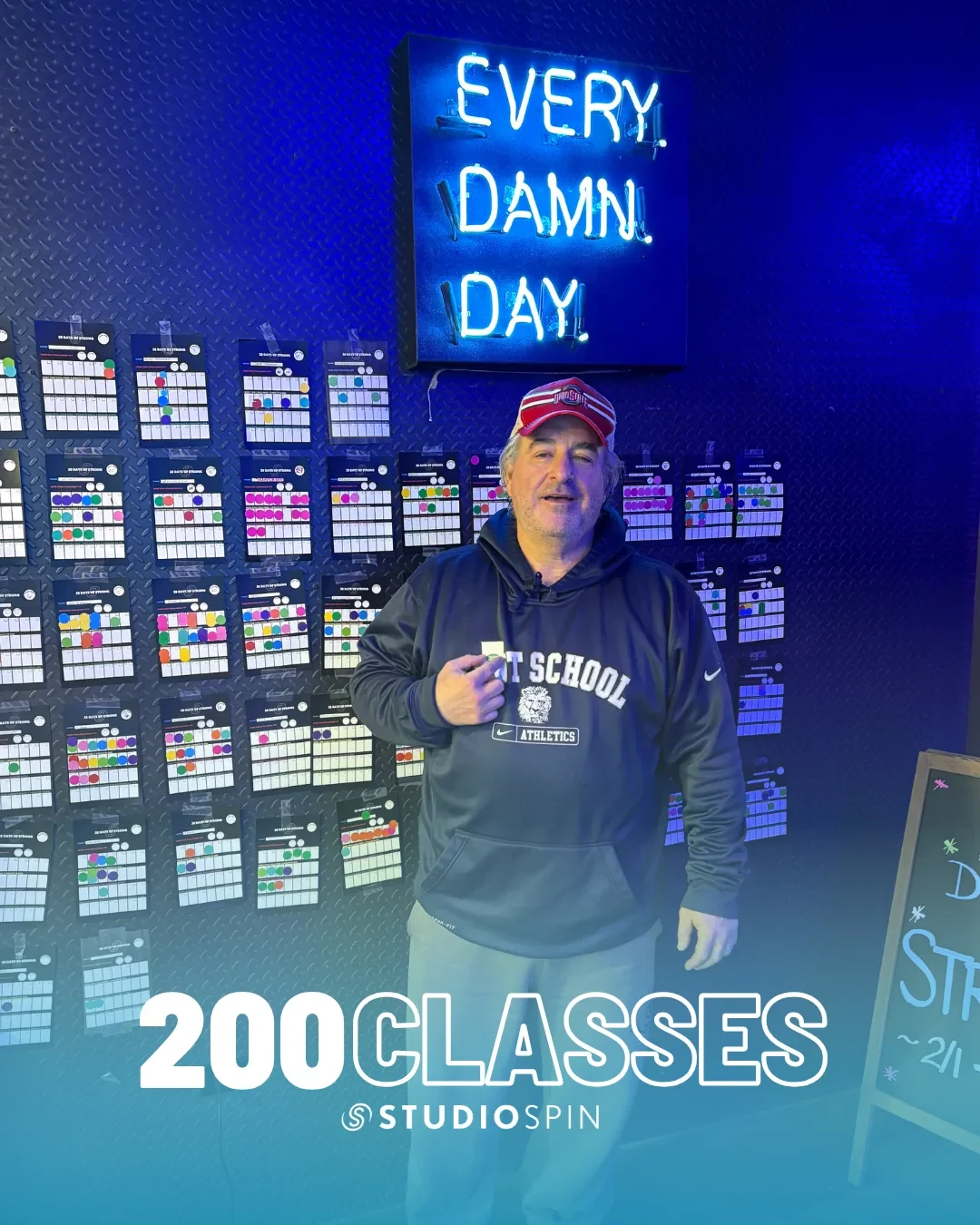 A Studio Spin member celebrating 200 classes under the Every Damn Day neon sign.