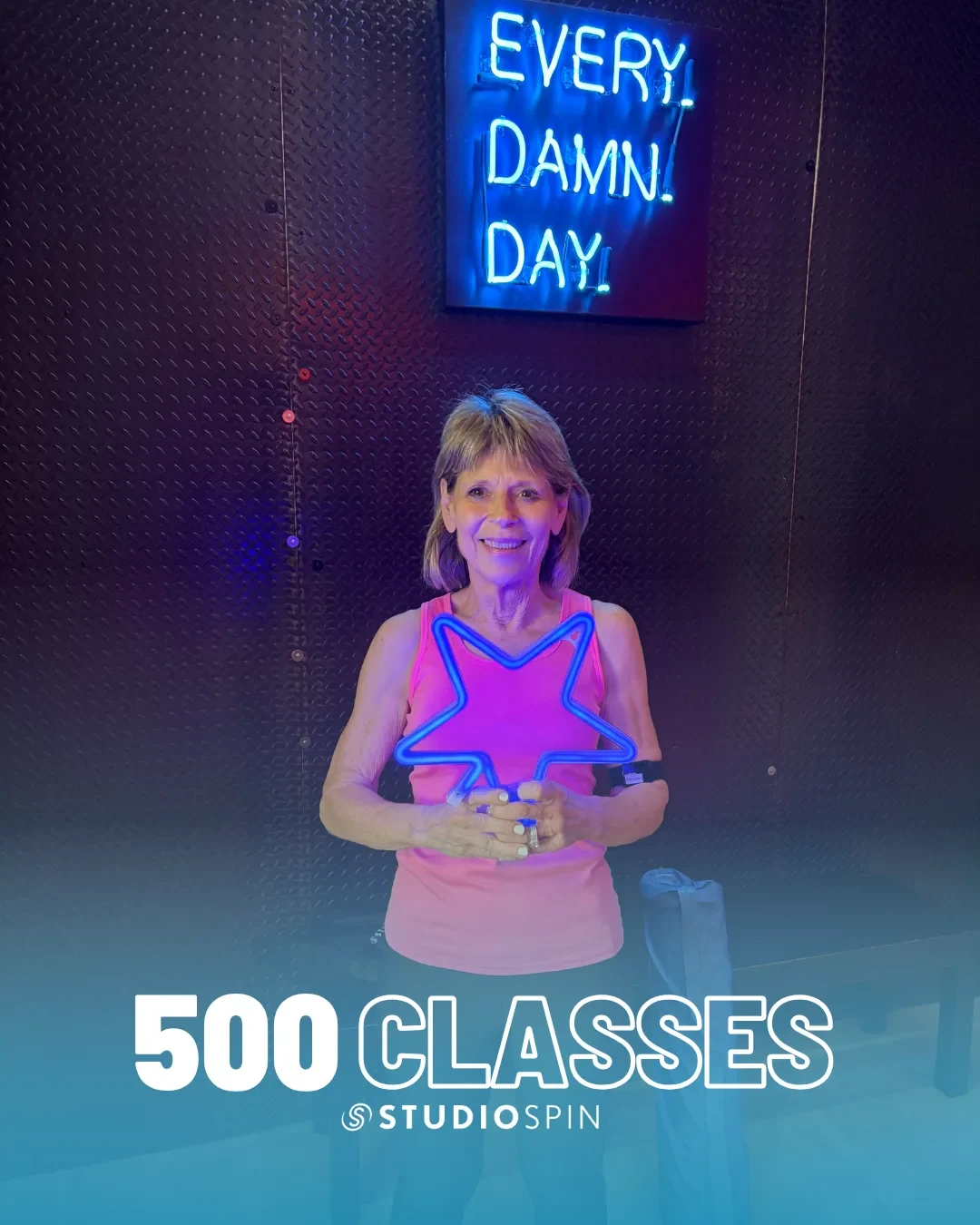 A Studio Spin member celebrating 500 classes under the Every Damn Day neon sign.