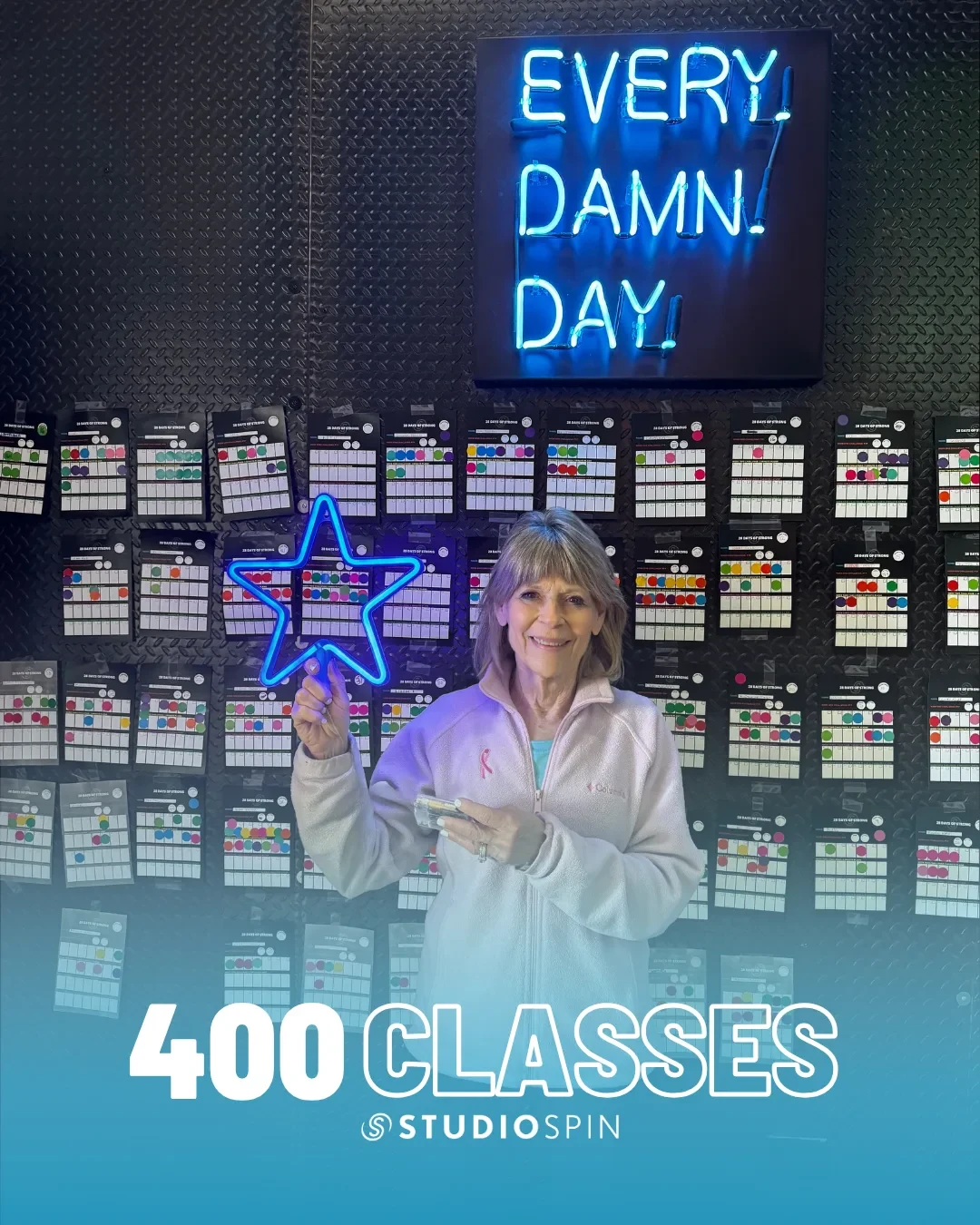 A Studio Spin member celebrating 400 classes under the Every Damn Day neon sign.