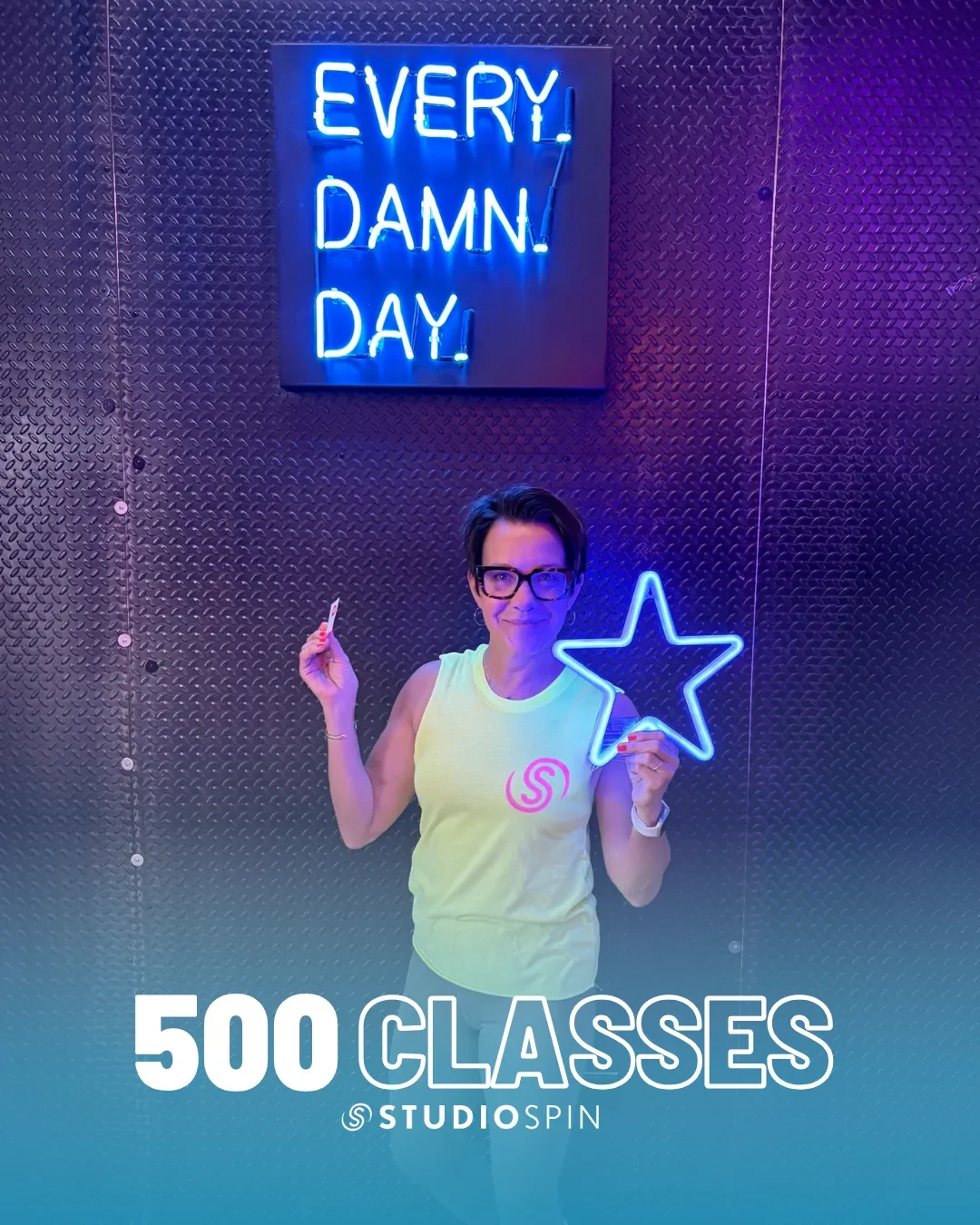 A Studio Spin member celebrating 500 classes under the Every Damn Day neon sign.