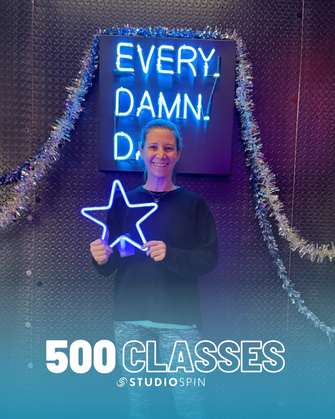 A Studio Spin member celebrating 500 classes under the Every Damn Day neon sign.