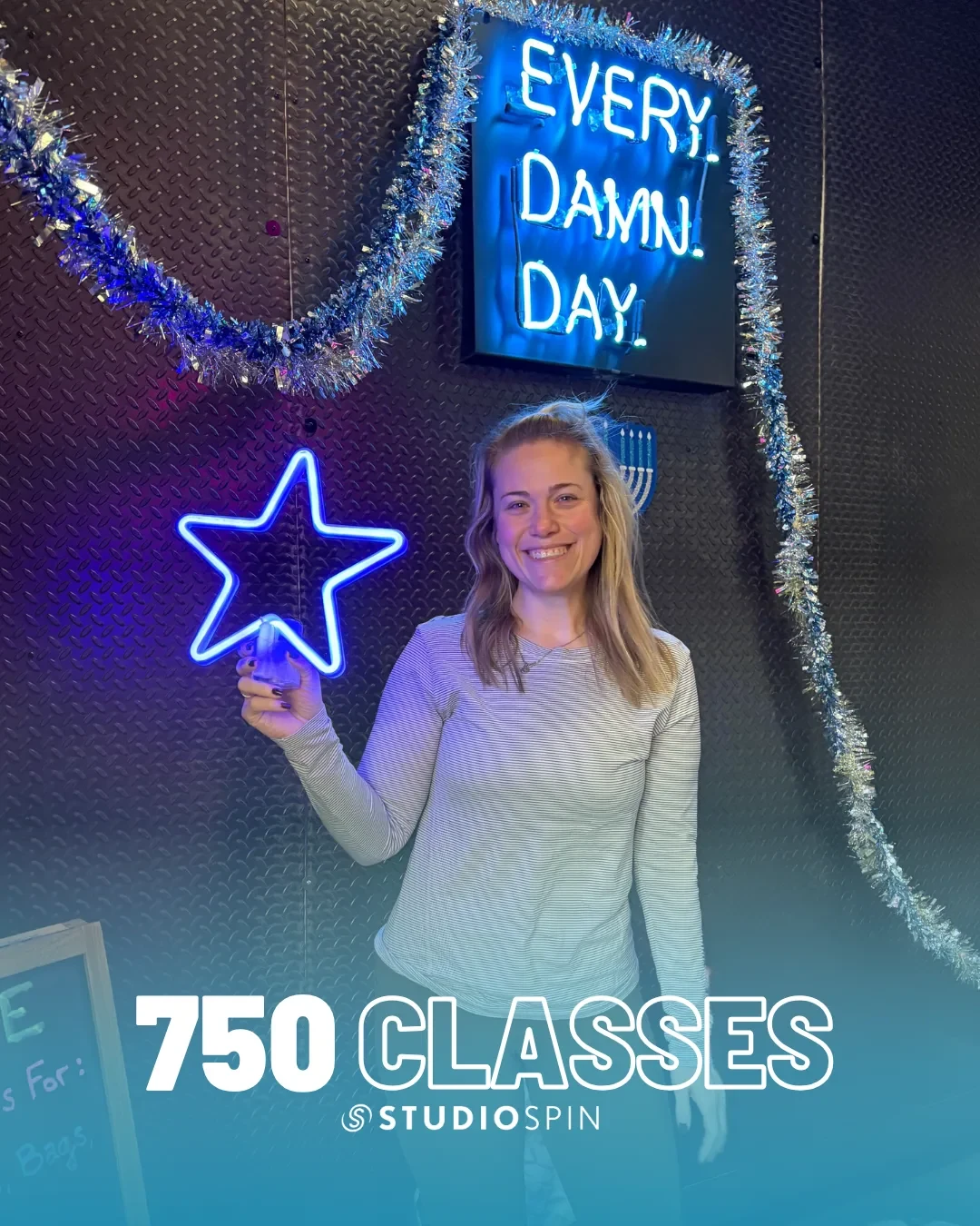 A Studio Spin member celebrating 750 classes under the Every Damn Day neon sign.