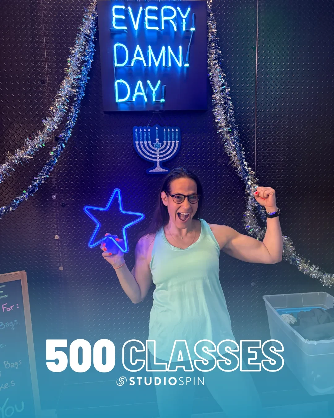 A Studio Spin member celebrating 500 classes under the Every Damn Day neon sign.