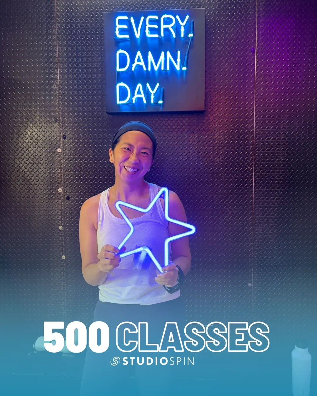 A Studio Spin member celebrating 500 classes under the Every Damn Day neon sign.
