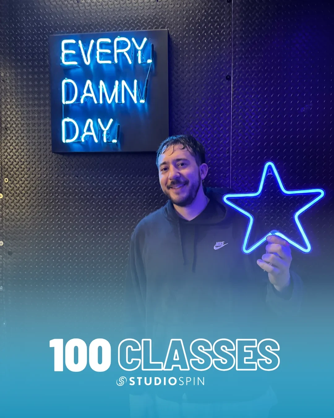 A Studio Spin member celebrating 100 classes under the Every Damn Day neon sign.