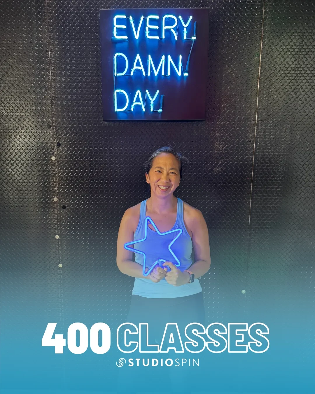 A Studio Spin member celebrating 400 classes under the Every Damn Day neon sign.